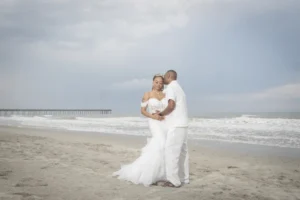 Newlyweds embracing on the beach beneath a soft evening sky