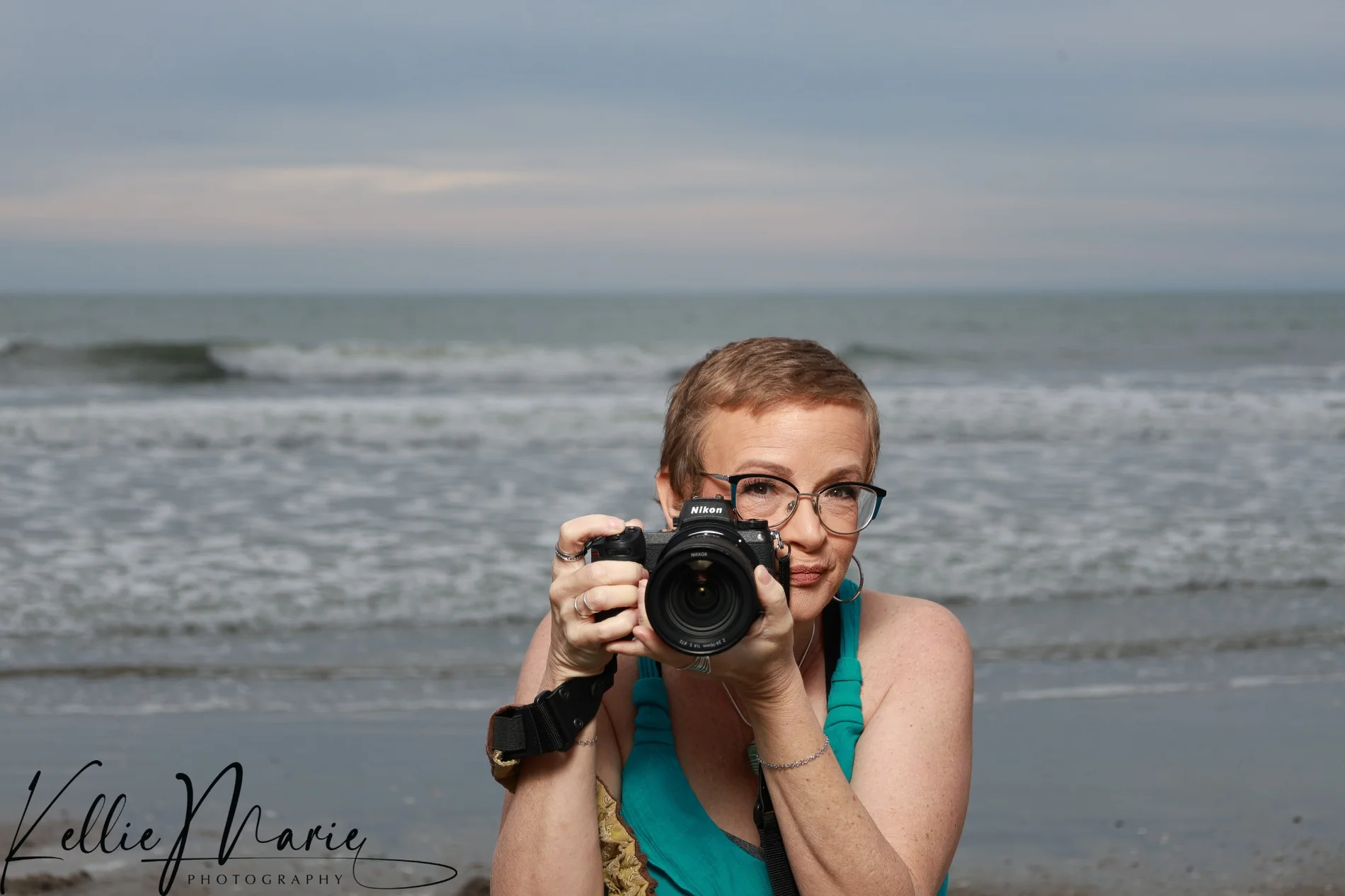 Casey holding her camera beside the ocean