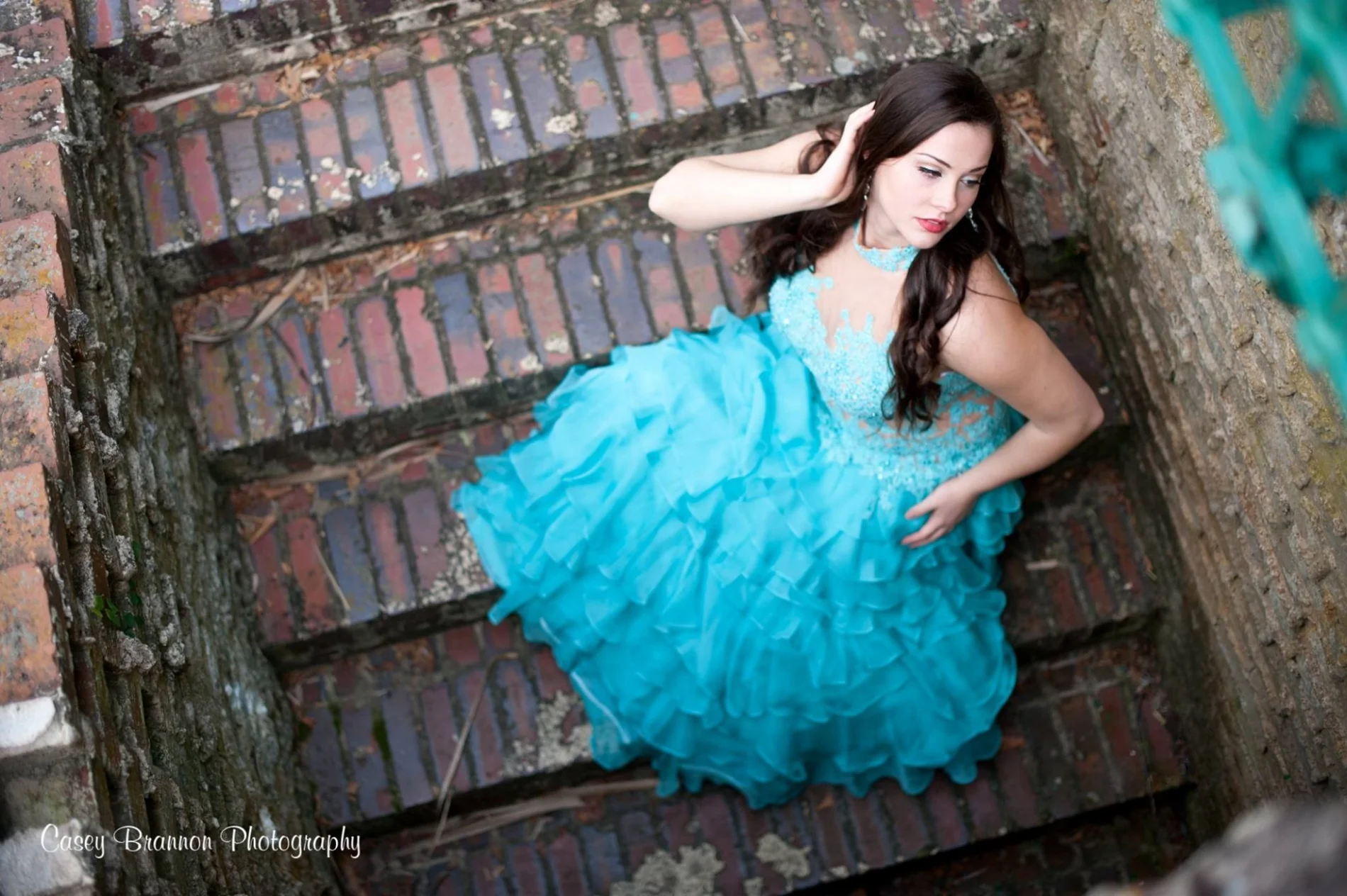 Senior portrait in a turquoise gown beside brickwork