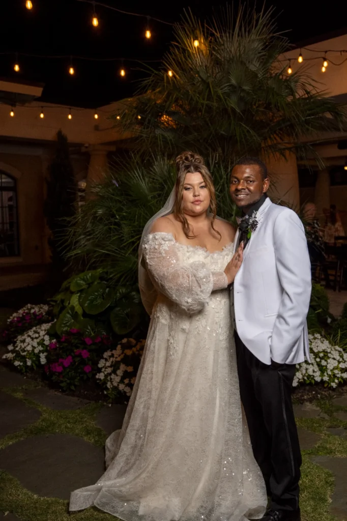 Wedding couple standing together beneath string lights