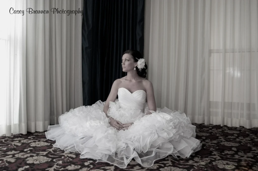 Bride seated by tall curtains in a monochrome portrait