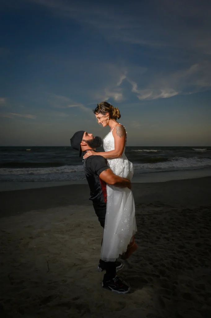 Newlyweds embracing at the water&rsquo;s edge at dusk