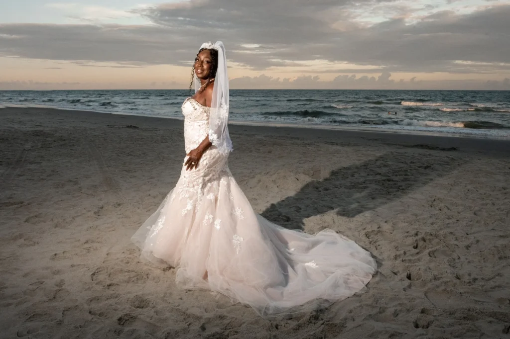 Bride with her gown spread over the sand at sunset