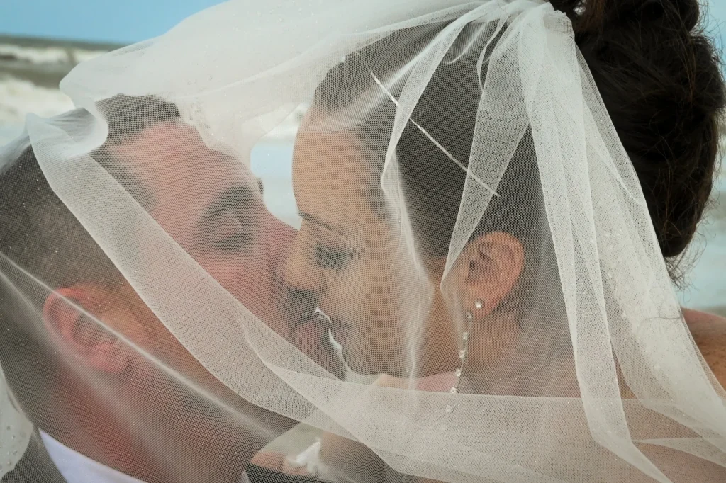 Wedding couple sharing a kiss beneath a veil