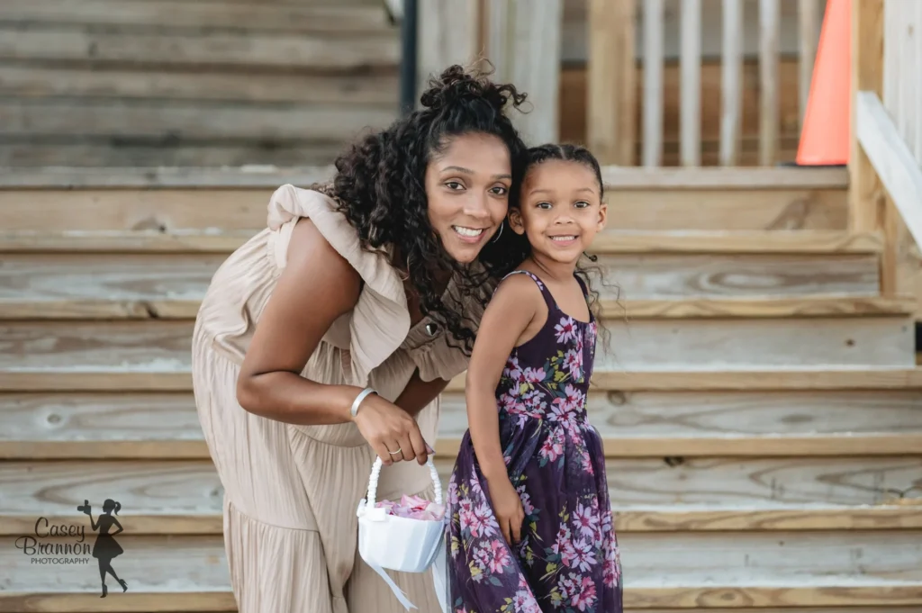 Bride smiling beside a young flower girl on wooden steps